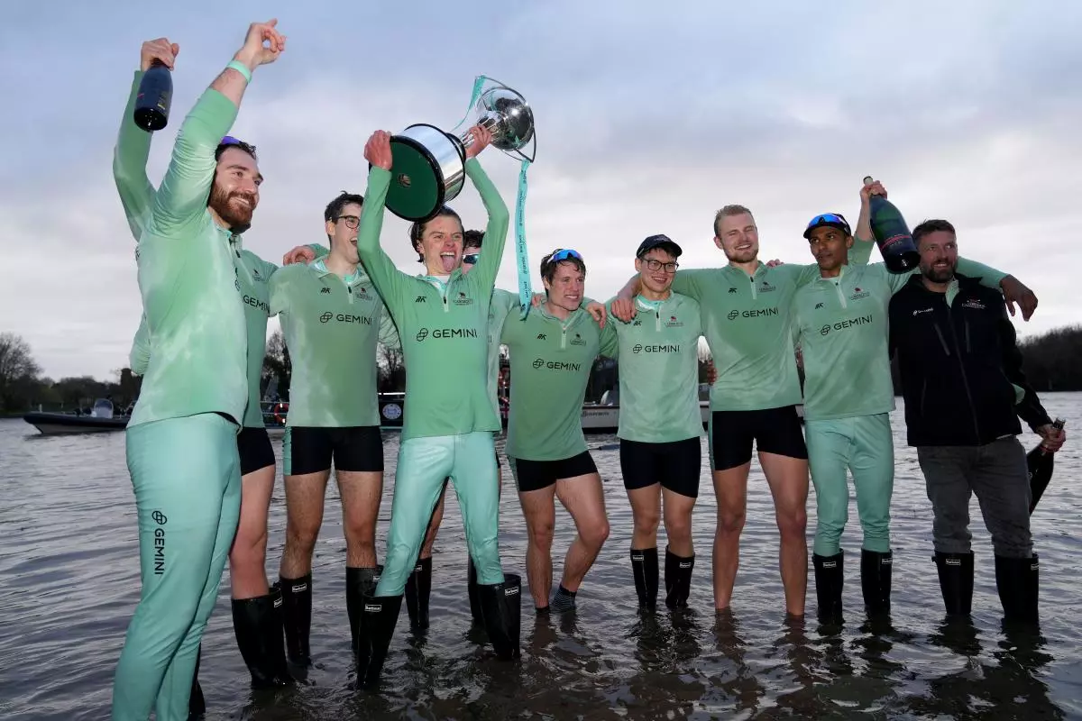 Cambridge men's cox Jasper Parish (centre) celebrates with the trophy