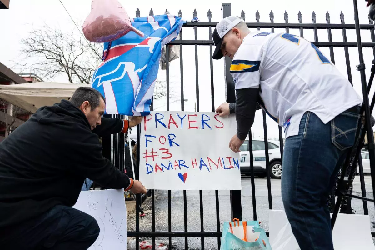 Football fans tape a sign to a fence during a vigil outside the University of Cincinnati Medical Center where Buffalo Bills safety Damar Hamlin was in critical condition
