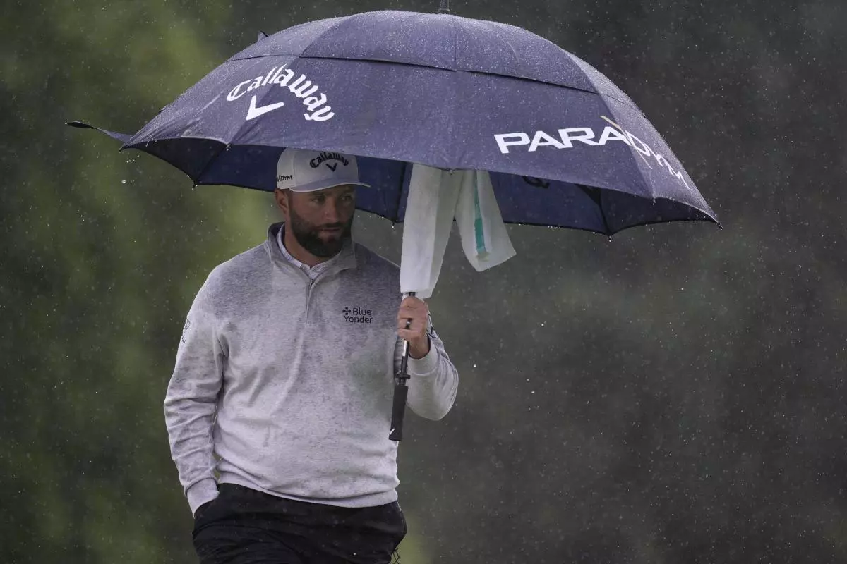 Jon Rahm protects himself from the rain at the 18th green during the rain delayed second round